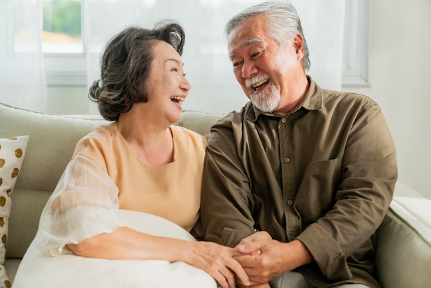 Free photo old senior asian retired age marry couple wellness lifesstyle together at homeold people laugh smile together with love and bonding on sofa in living room home interior background