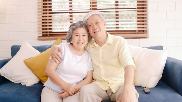 Free photo asian elderly couple watching television in living room at home, sweet couple enjoy love moment while lying on the sofa when relaxed at home.