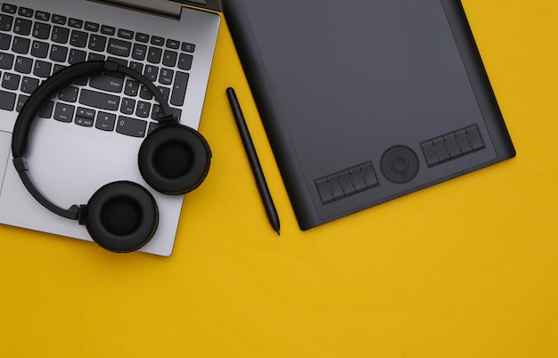 Photo workspace of retoucher or graphic designer. laptop, graphic tablet and headphones on yellow background. top view.